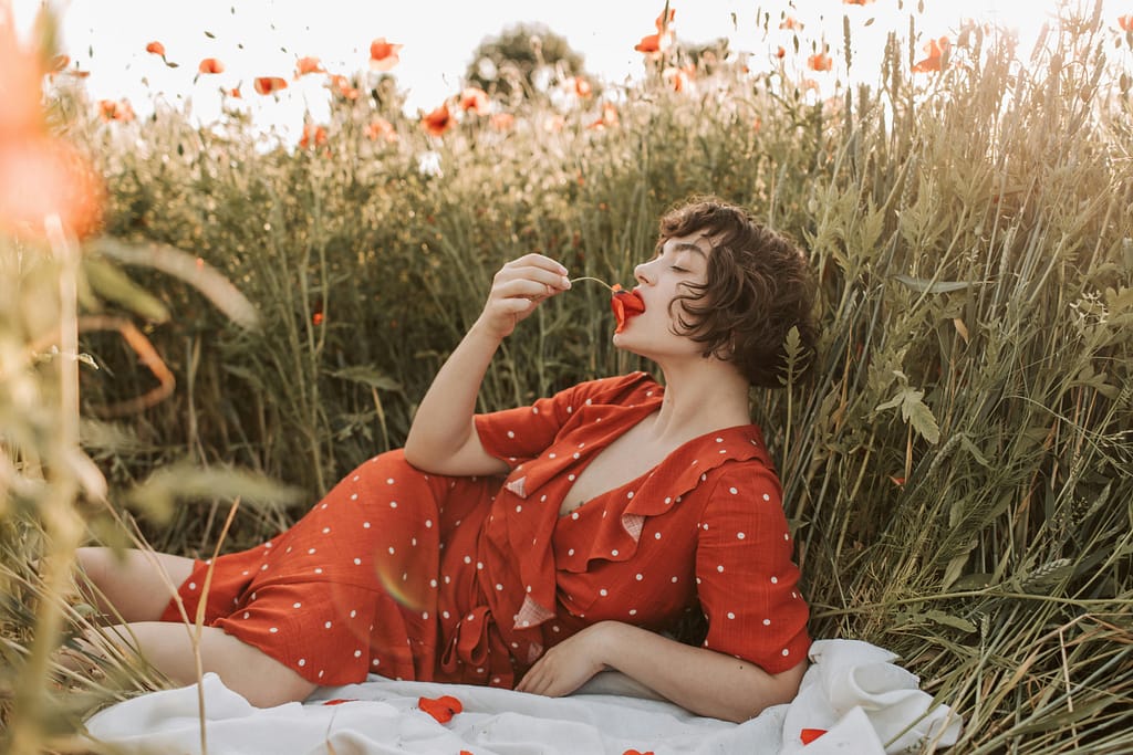 Illustre l'article sur les Fleurs de Bach. A woman enjoys a serene moment in a poppy field, dressed in a red polka dot dress.